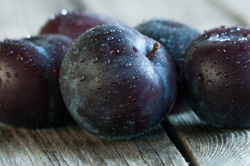 Dark plums close-up with water drops on wooden boards. Selective focus at shallow depth of field