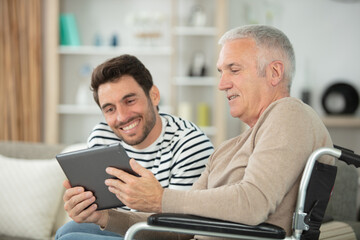 happy handsome father in wheelchair and son using tablet