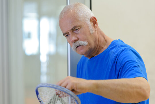 senior man inspecting racket before match