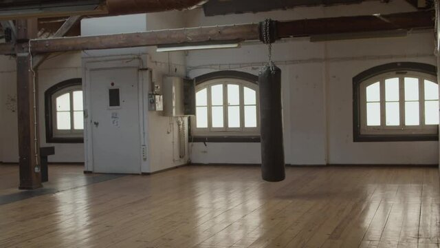 Long shot of empty kickboxing gym with swinging punching bag. Horizontal shot of boxing room for sportsmen and athletes in daytime. Sport, training concept