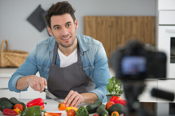 camera filming young smiling male blogger at the kitchen