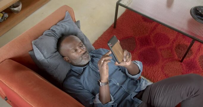 Single black male using smart phone browsing social media at home on sofa