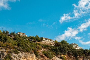 Fototapeta na wymiar Scenic vibrant landscape with Greek recreation villa houses on green high hills on blue scenic sky with clouds and young moon on Lefkada island, Greece. Travel in summer