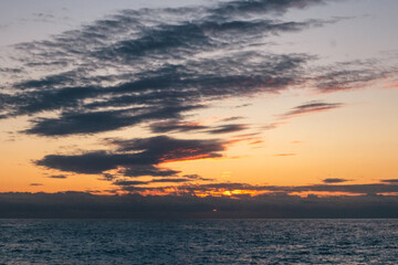 Naklejka na ściany i meble Sunset sky with dark purple clouds above blue rippled sea water. Dramatic cloudscape on Mediterranean sea