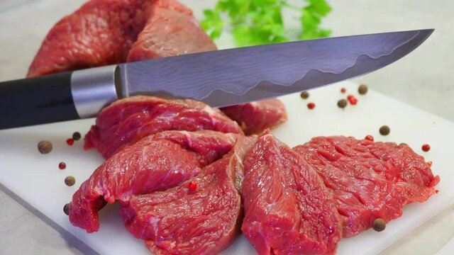 A damask steel knife with a pattern cuts red meat. Chopped beef, slices, abolition of vegetarianism, semi-finished meat products, soy meat