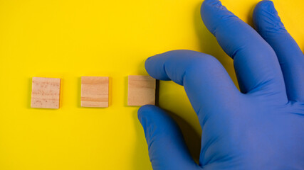 Hand in blue gloves point on clean wooden blocks on colored yellow background. Medical scientific or biological theme. Template for text or concept. Advertising mock up. Presentation flat lay mock up