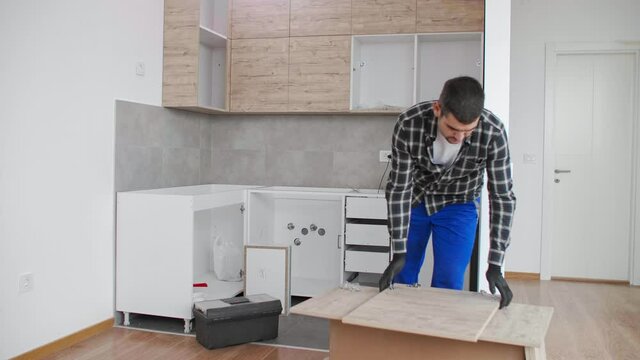 The carpenter screwing in and mounting hinge on kitchen shelves.