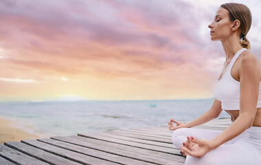 Yoga and meditation. Closeup of young woman in lotus pose on wooden deck with sea view.