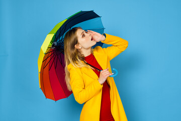 woman in yellow coat multicolored umbrella posing blue background