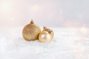 A variety of golden shiny Christmas balls on the snow on a light background.