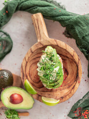 Top view of Russian salad with avocado and coriander sprouts on wooden plate.