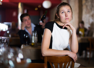 Sad woman sitting apart in restaurant with drunk man behind