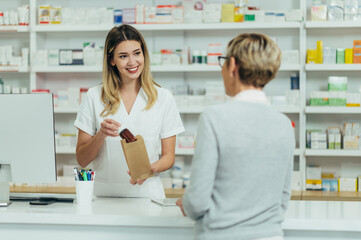 Female pharmacist selling medications at drugstore to a senior woman customer