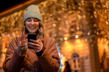 Young woman using a smartphone outside with the decorative christmas lights in the background