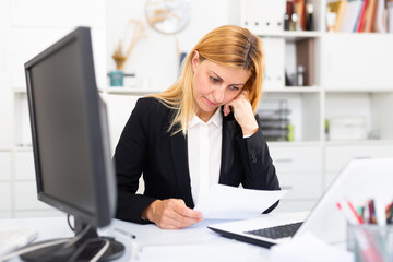 Fototapeta na wymiar Frustrated businesswoman working alone with papers and laptop in business office