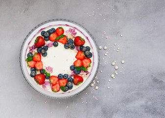 Delicate cake garnished with fresh strawberries blueberries on a gray plain background. Festive dessert with berries