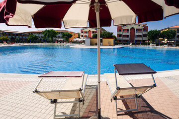 Fototapeta premium Resort pool. Summer resort chair, relax lounge at luxury hotel pool. Beach lounger chaise. Vacation sunbed. Blue water, sunny happy travel holiday.