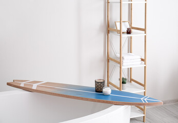 Bathtub with surfboard and aroma candles in modern interior of bathroom
