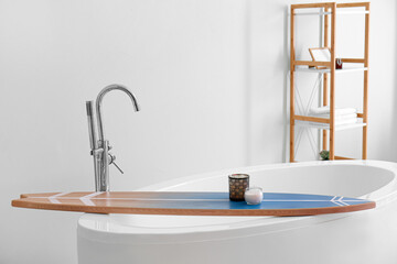 Bathtub with surfboard and aroma candles in modern interior of bathroom