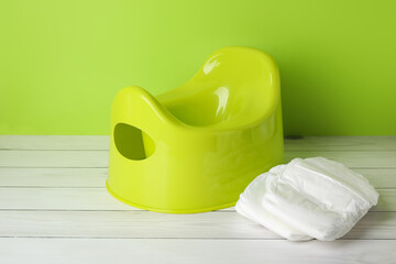 Potty and diapers on white wooden floor near color wall