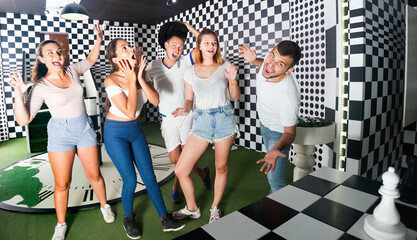 Group of young smiling cheerful people having fun in escape room stylized under chessboard