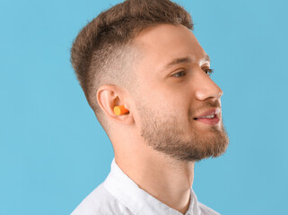 Young man with ear plug on blue background