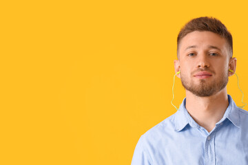 Handsome young man with ear plugs on yellow background