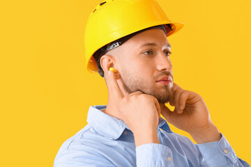 Young man with hardhat and ear plugs on yellow background
