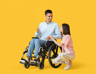 Young man in wheelchair and his wife on color background