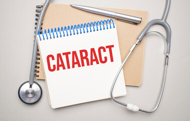 White notepad with the words cataract and a stethoscope on a blue background. Medical concept