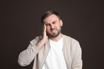 Young man suffering from headache on dark background