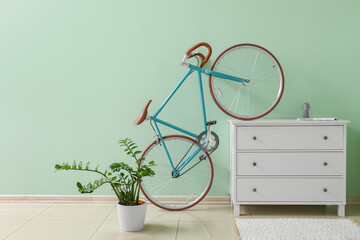 Modern bicycle with chest of drawers and houseplant near green wall