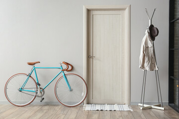 Modern bicycle and rack with clothes near light wall in hall