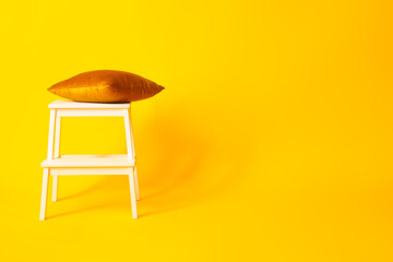 White step stool with pillow on yellow background
