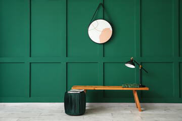 Wooden bench with decorative moss, lamp and pouf near green wall