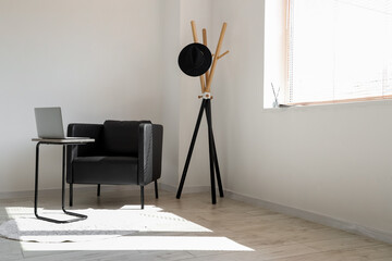 Table with laptop, black armchair and stand near light wall