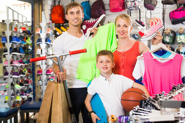 Happy friendly parents with boy in school age shopping clothing in sport store. Focus on woman