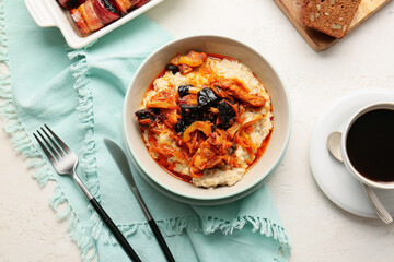 Bowl with delicious oatmeal, beef stew, prunes, cutlery and cup of coffee on light table