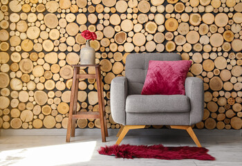 Grey armchair and vase with flowers on stool near wooden wall