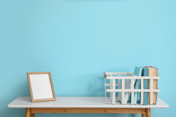 Basket with books and frame on table near blue wall