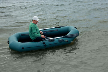 Obraz premium Man fishing with rod from inflatable rubber boat on river