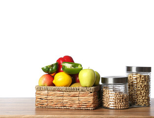 Basket with food and jars of cornflakes on wooden table top against white background