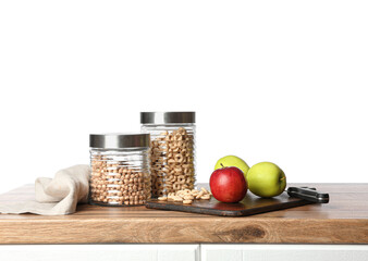Jars of cornflakes, apples, board and knife on table top against white background