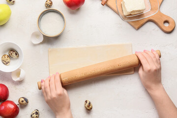 Woman rolling out dough for preparing apple strudel on white background
