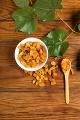 Bowl with tasty raisins and branch on wooden background