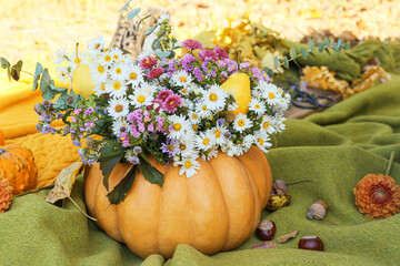 Beautiful bouquet of autumn flowers in pumpkin on warm plaid outdoors