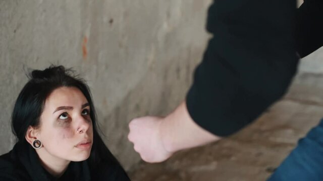 Kidnapped woman sitting and threatened by man with knife in hands in abandoned building