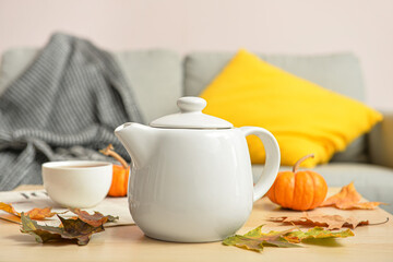 Tea pot and autumn leaves on table in room