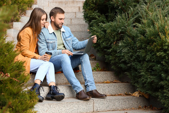 Young couple with laptop sitting on stairs in autumn park