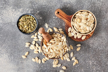 Bowls with natural pumpkin seeds on grey background
